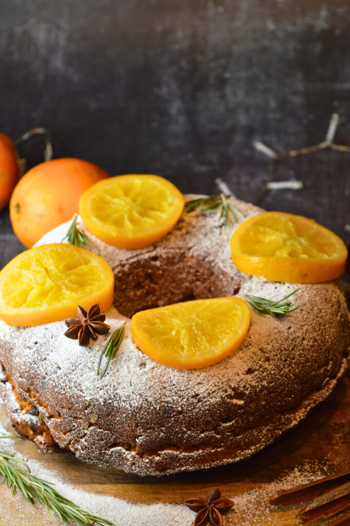Mince Pie Bundt Cake with Orange and Amaretto Glaze, Garnished with Powdered Sugar and Candied Orange Slices on a Festive Table