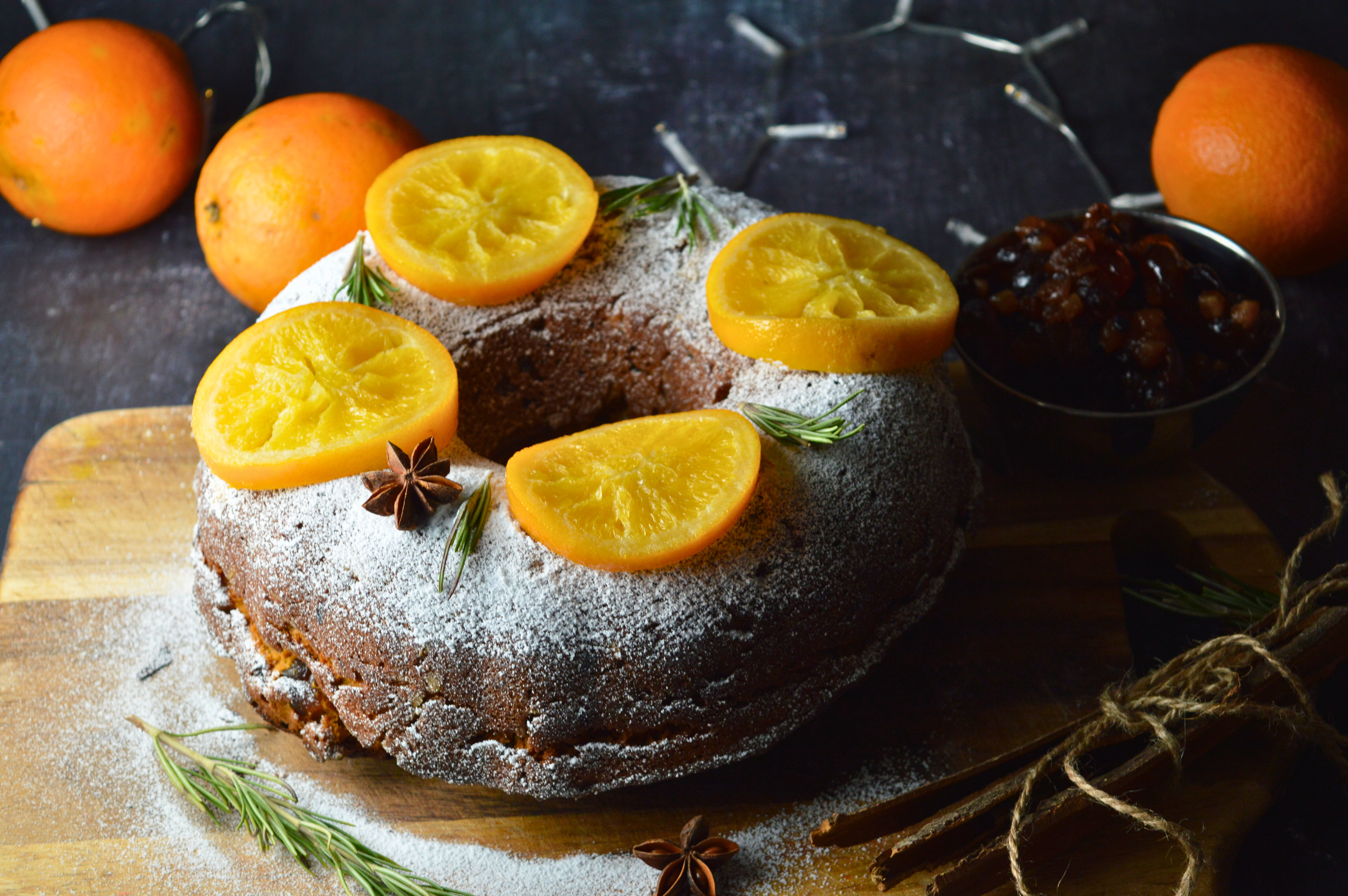 Mince Pie Bundt Cake with Orange and Amaretto Glaze, Garnished with Powdered Sugar and Candied Orange Slices on a Festive Table