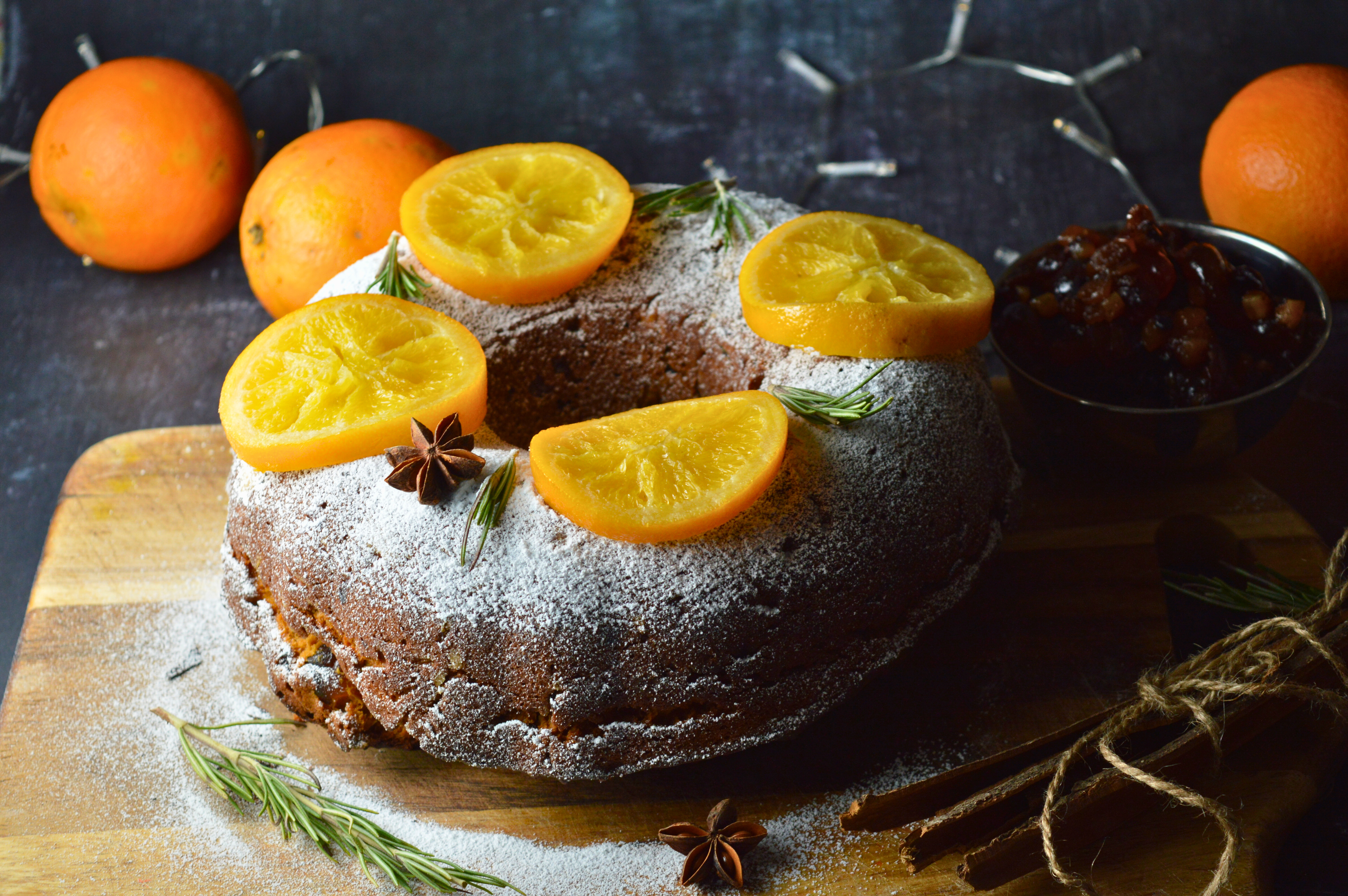 Mince Pie Bundt Cake with Orange and Amaretto Glaze, Garnished with Powdered Sugar and Candied Orange Slices on a Festive Table