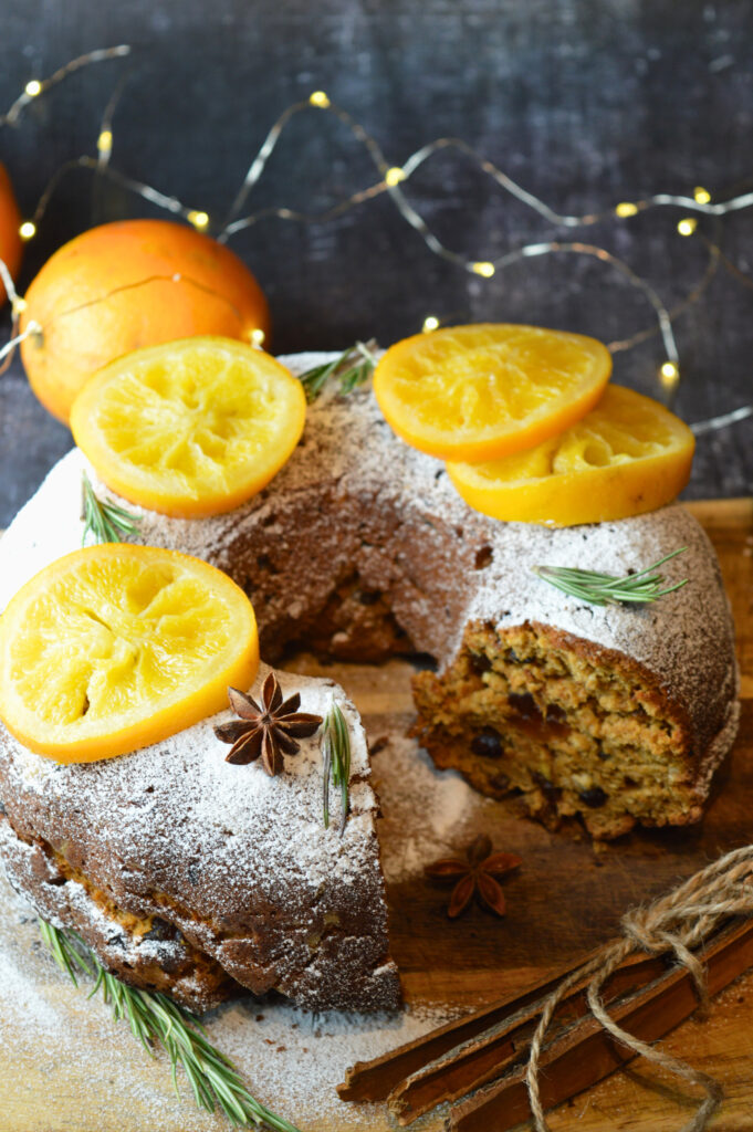 Mince Pie Bundt Cake with Orange and Amaretto Glaze, Garnished with Powdered Sugar and Candied Orange Slices on a Festive Table